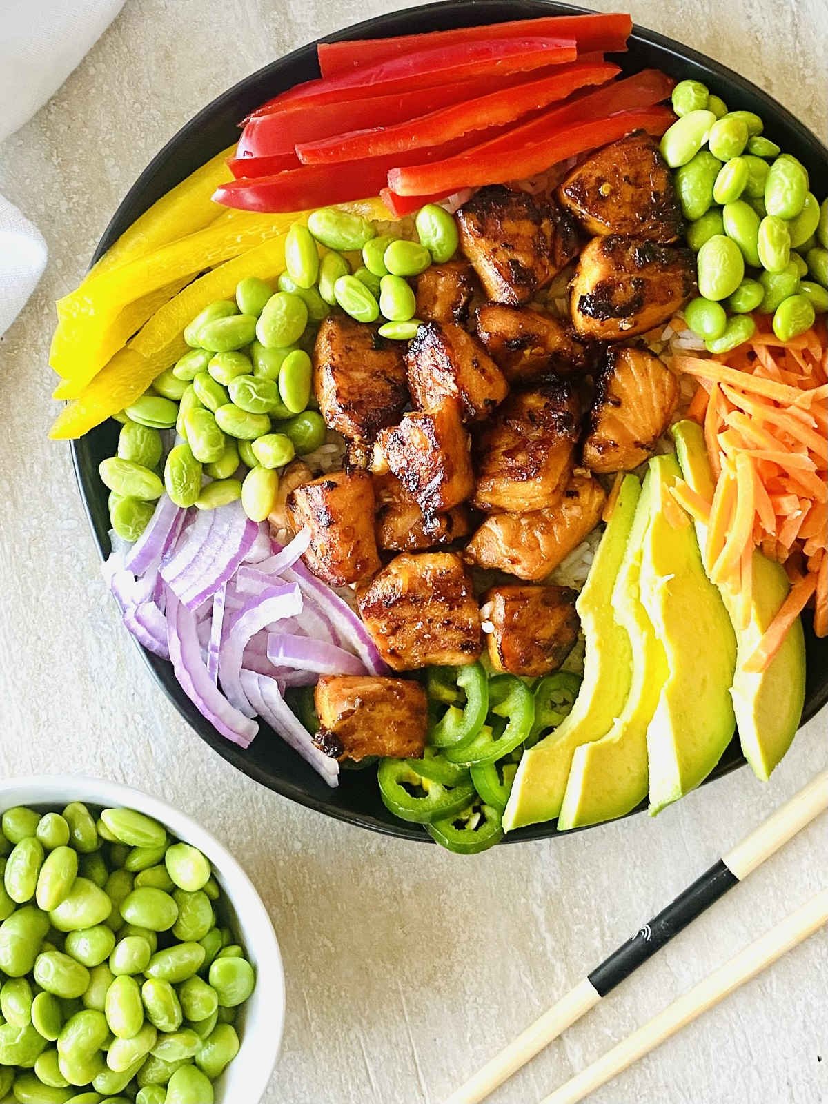 salmon rice bowl next to chopsticks and edamame