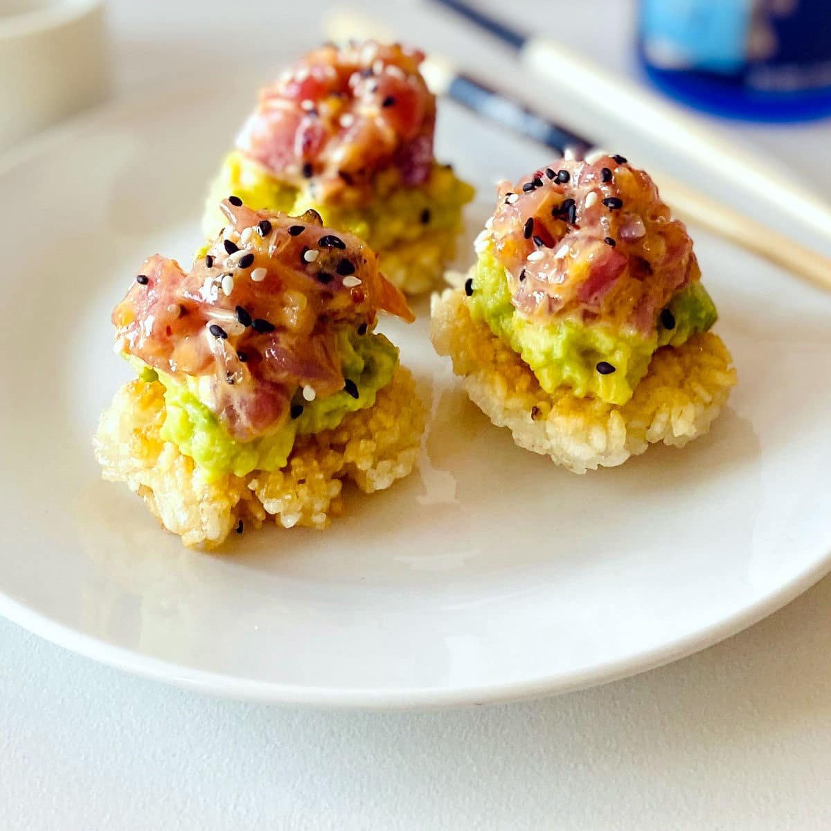 spicy tuna crispy rice on plate next to chopsticks, sake and sake carafe and glasses