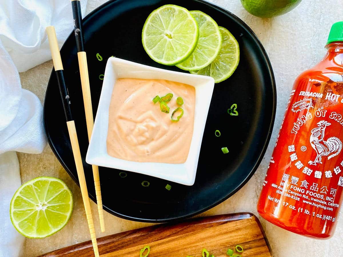 sriracha lime aioli in a dish next to a bottle of Huy Fong Sriracha Hot Chile Sauce and sliced limes.