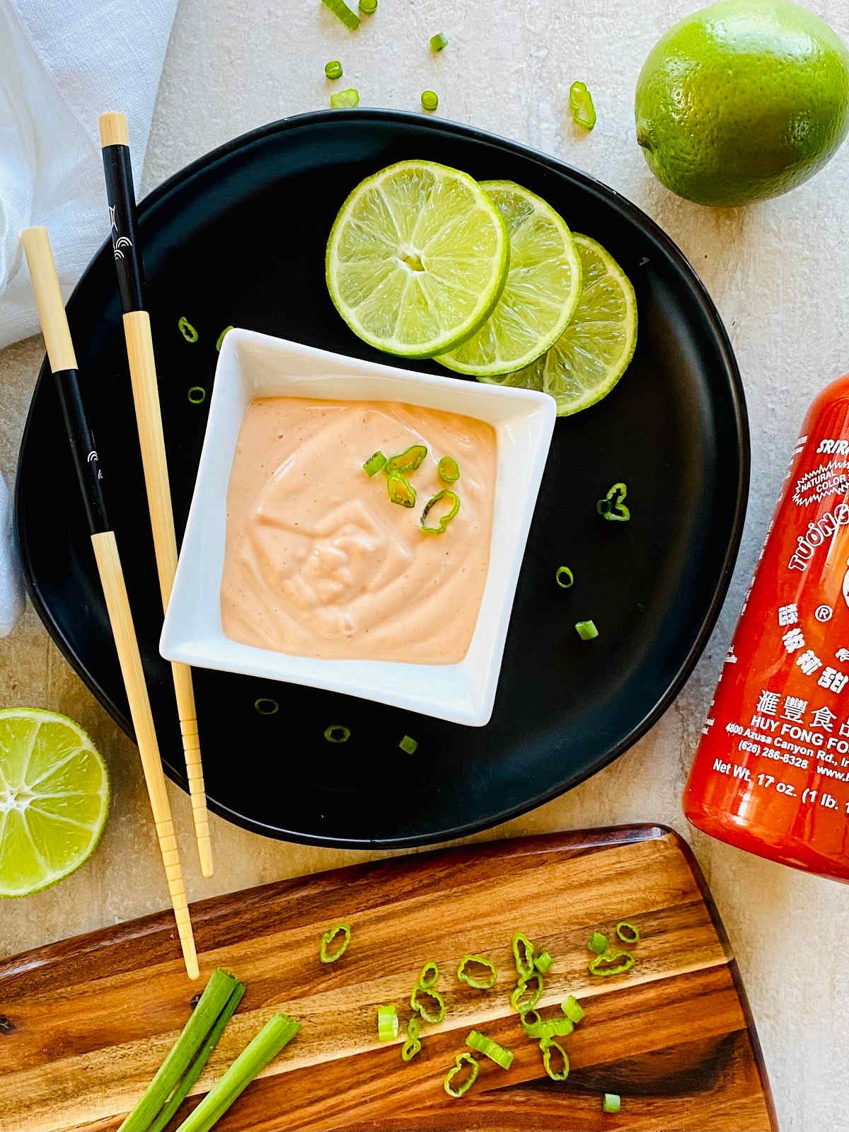 sriracha aioli sauce in a dish next to a bottle of Huy Fong Sriracha Hot Chile Sauce.