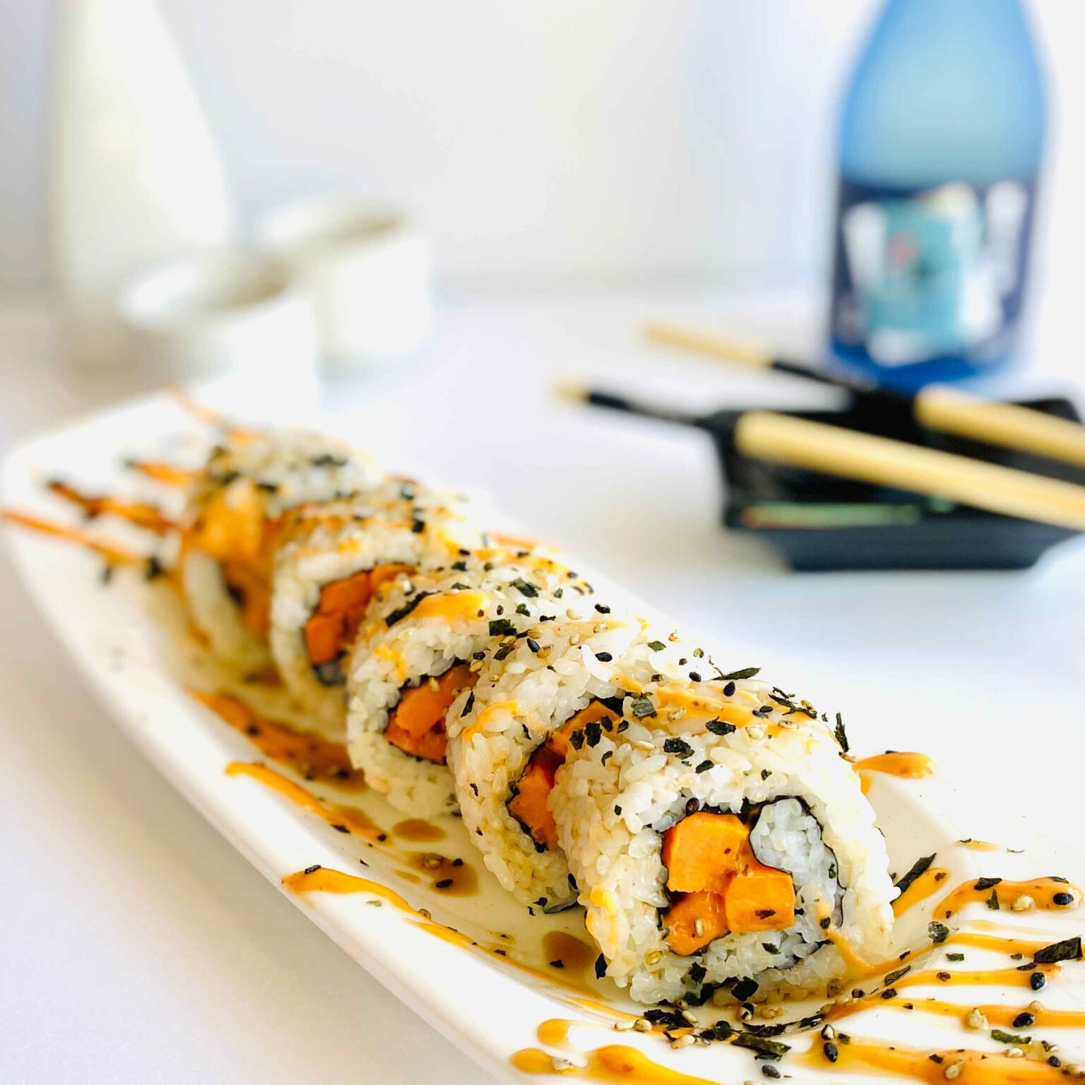 sweet potato sushi roll on plate with sake bottle and chopsticks in background