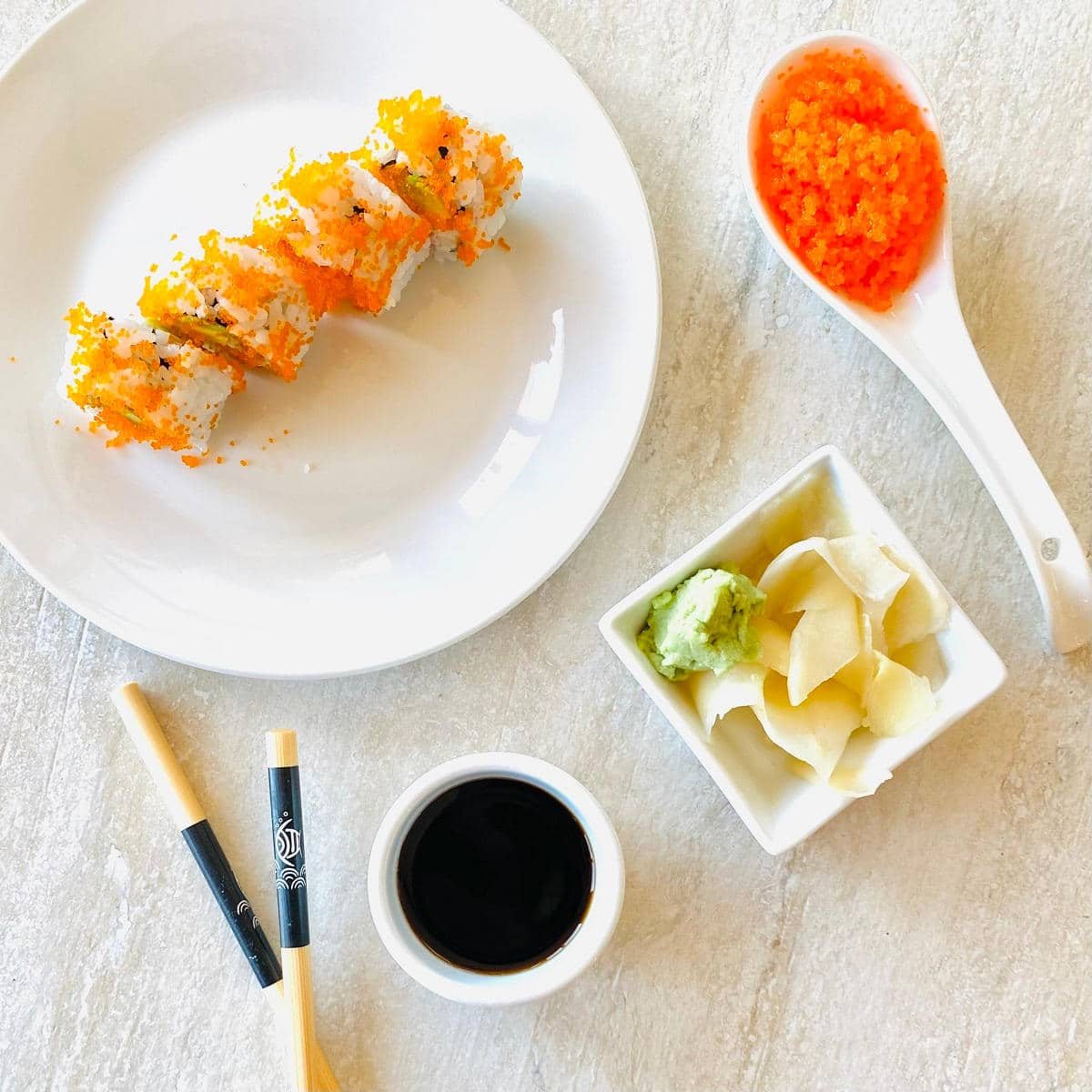 tobiko sushi recipe on a plate next to tobiko, soy sauce, ginger, wasabi and chopsticks