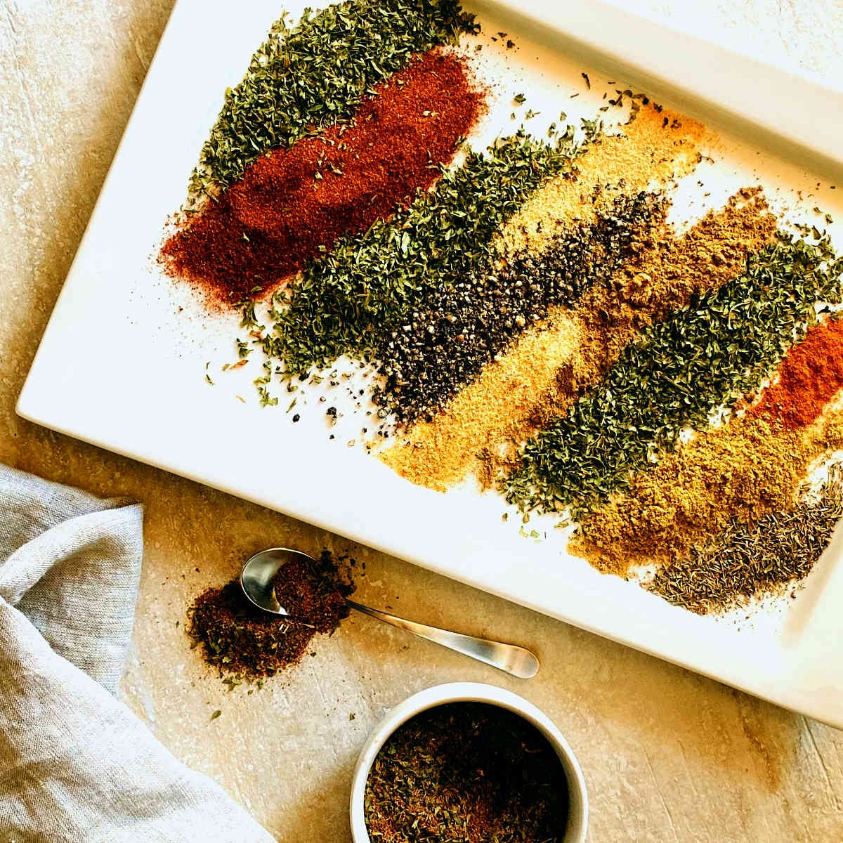 Tempero baiano brazilian spices layered next to each other on a white plate next to a dish of mixed seasoning and a spoonful
