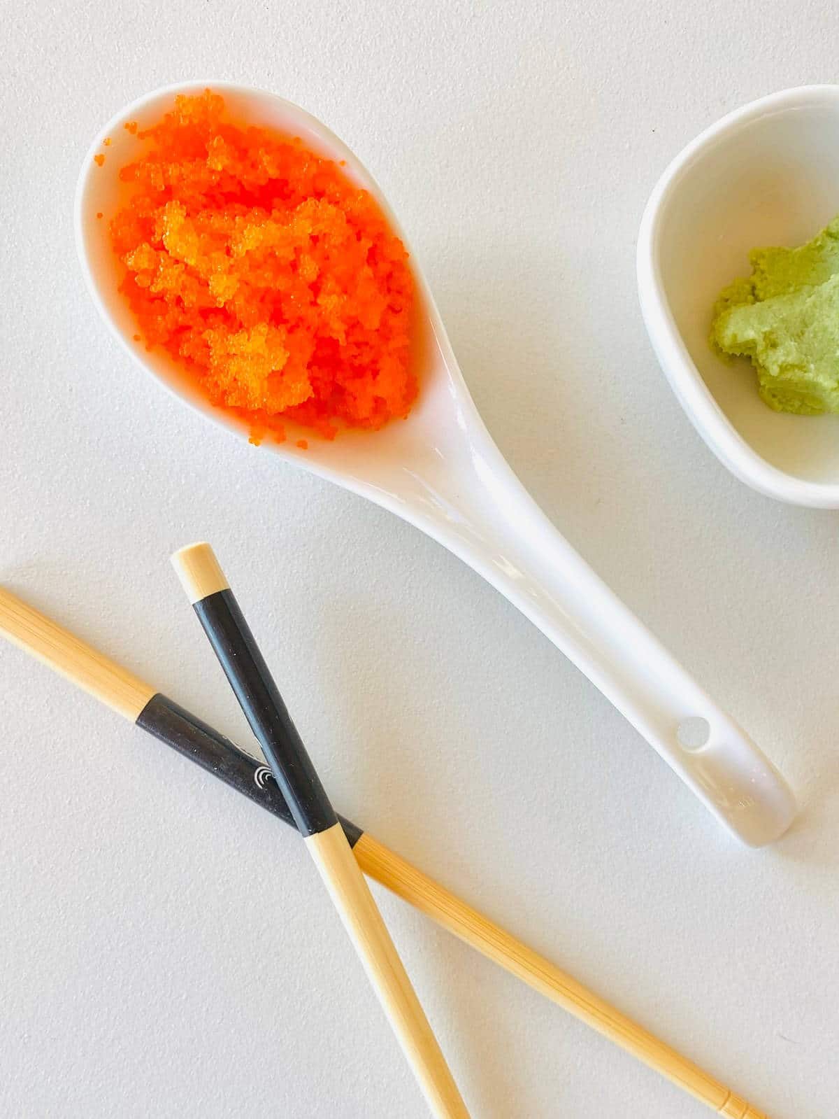 tobiko fish eggs in a spoon next to chopsticks and wasabi