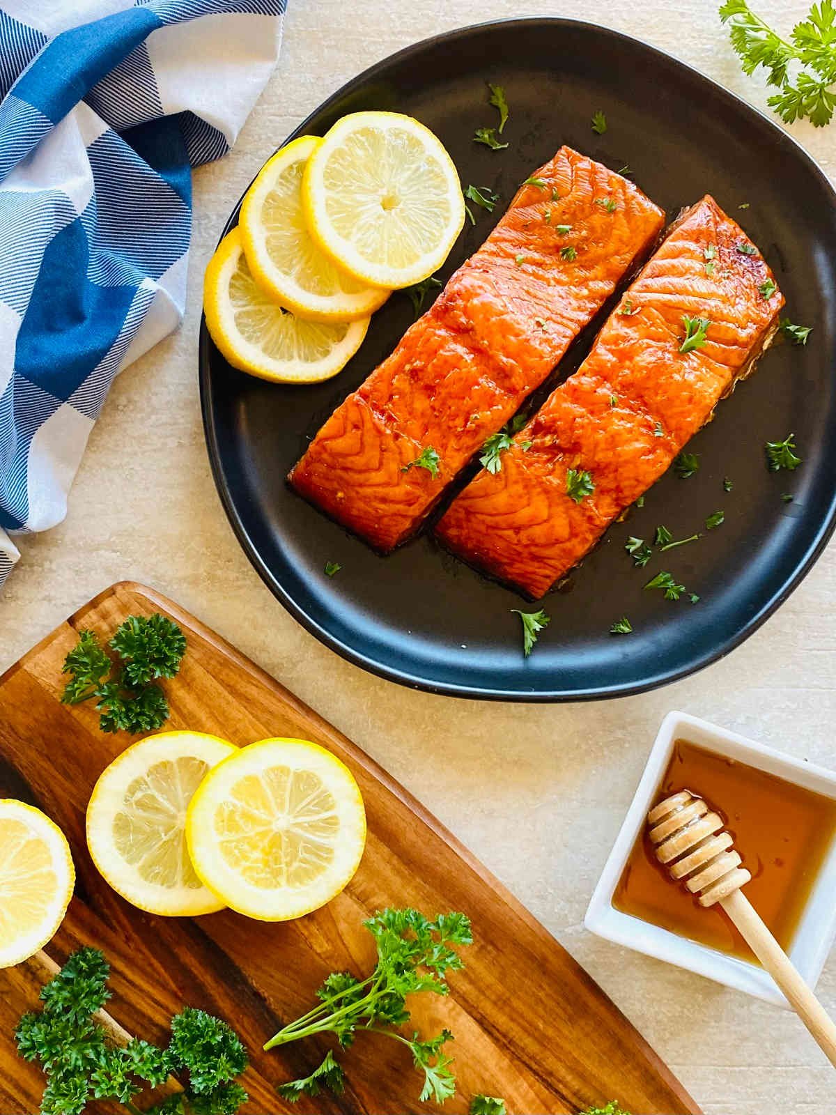 pellet grill smoked salmon on a black plate with sliced lemons and a side of honey.