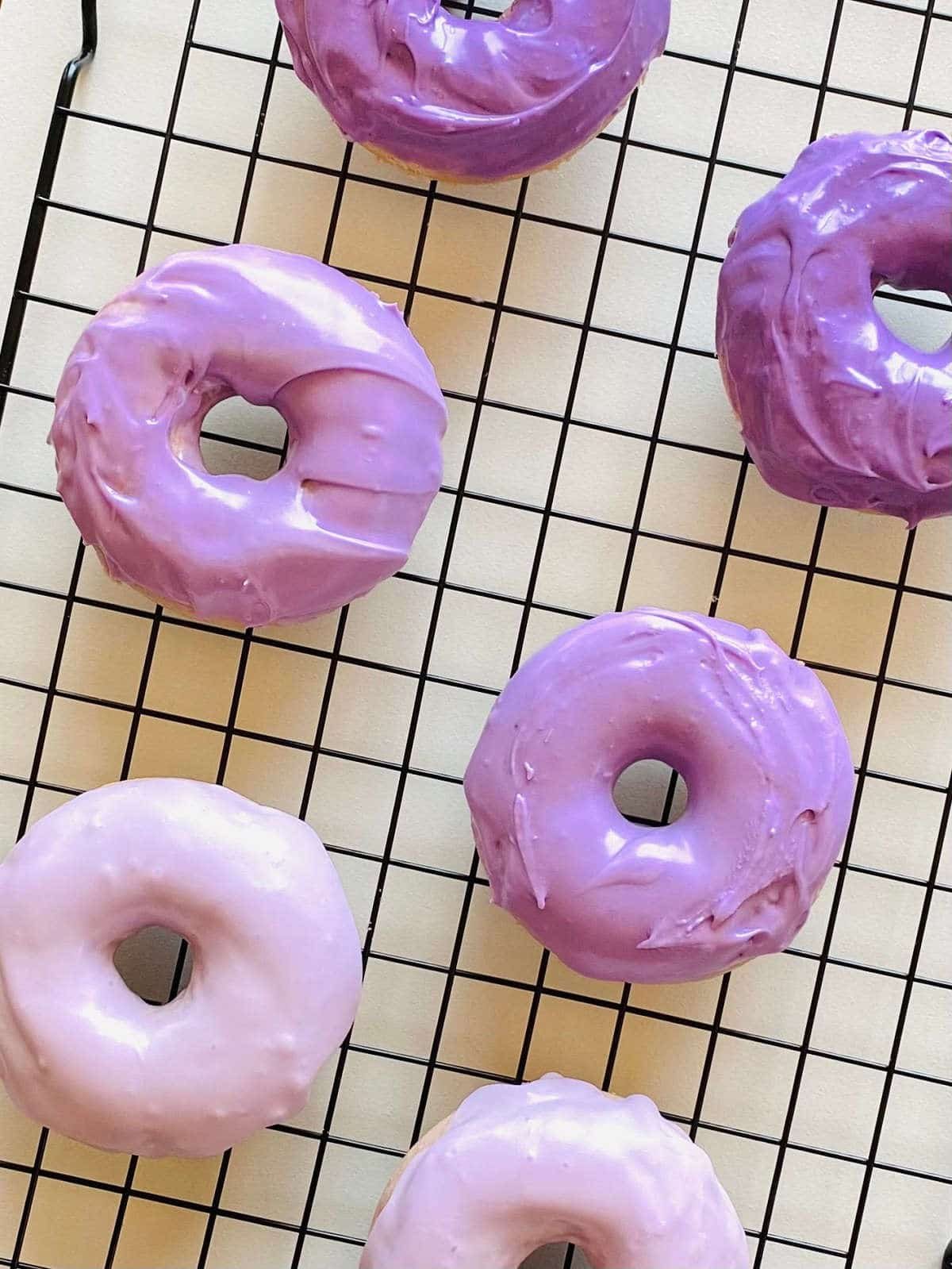 ube donuts on a black cooling rack