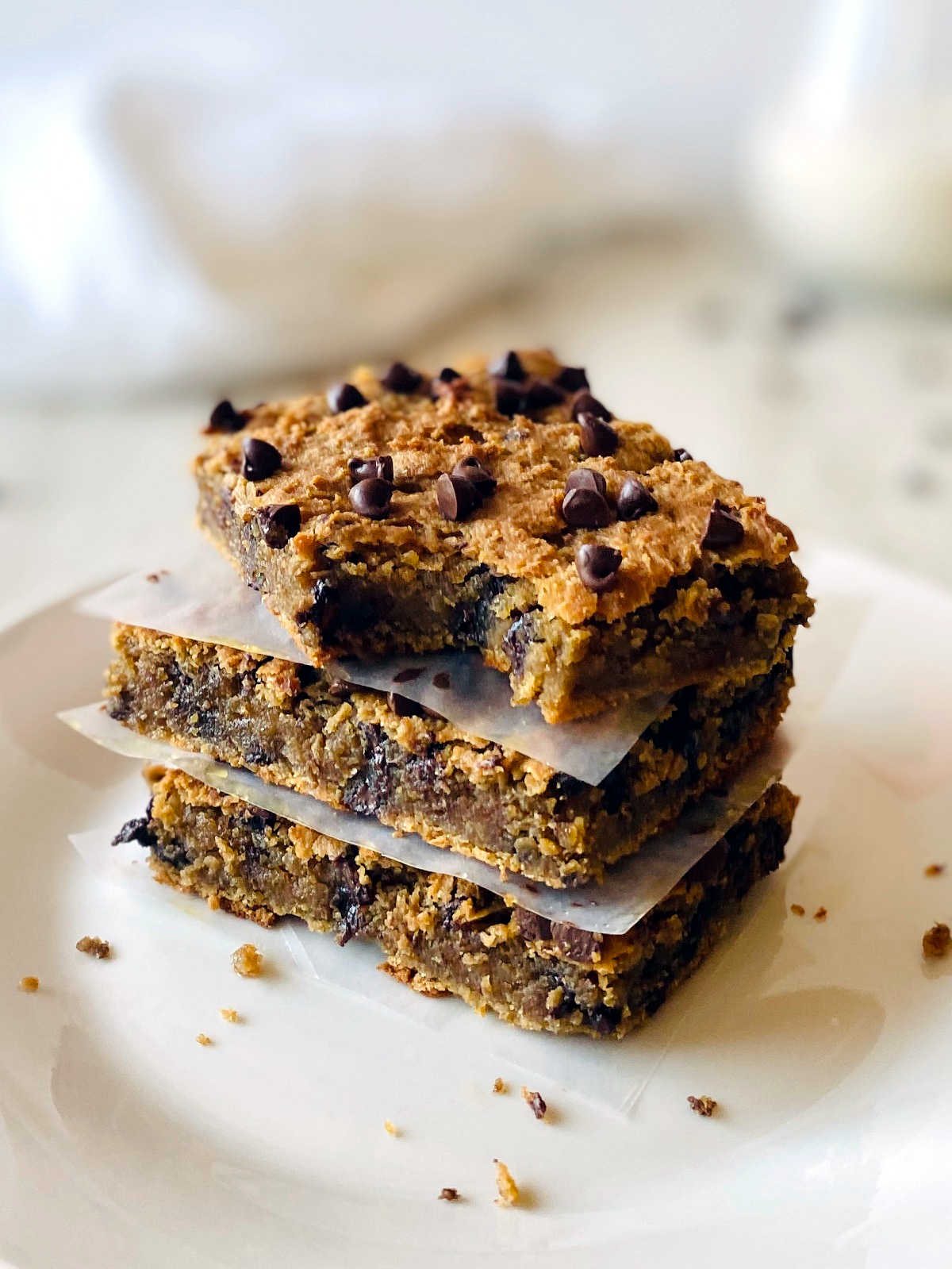 vegan blondies in a stack separated by parchment paper on a white plate with a bite out of the top blondie