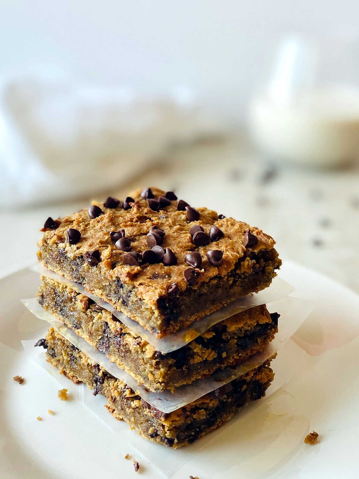 vegan blondies in a stack separated by parchment paper on a white plate