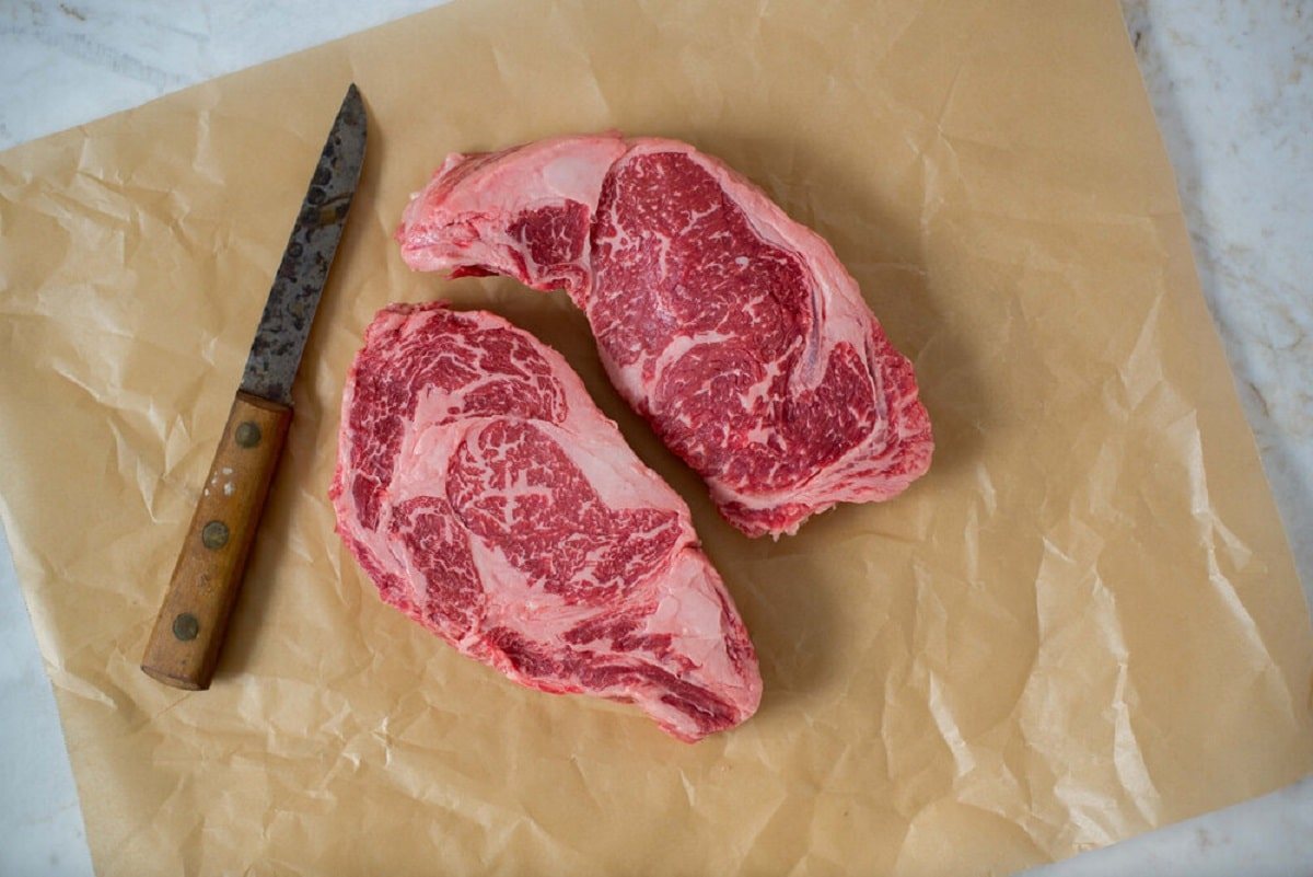 two american wagyu steaks on butcher paper next to a knife