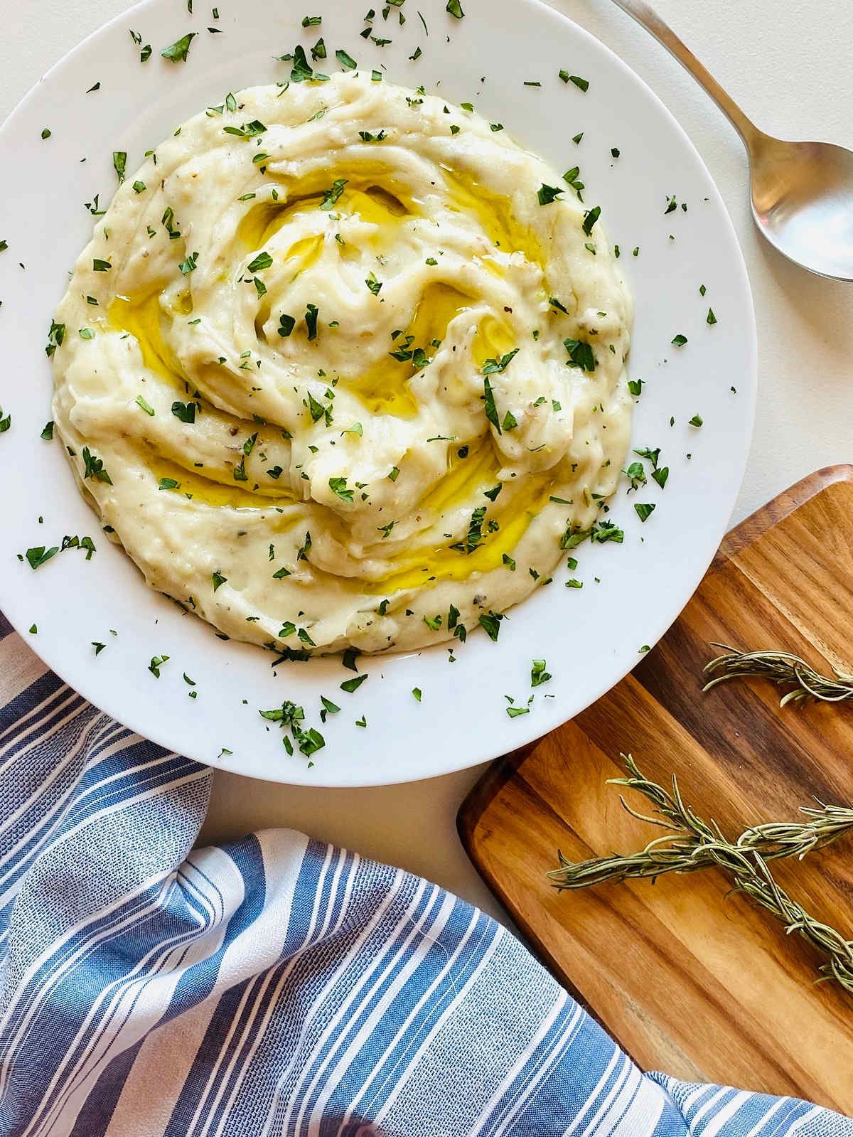 whole30 garlic mashed potatoes in white bowl with ghee on top next to knife and cutting board