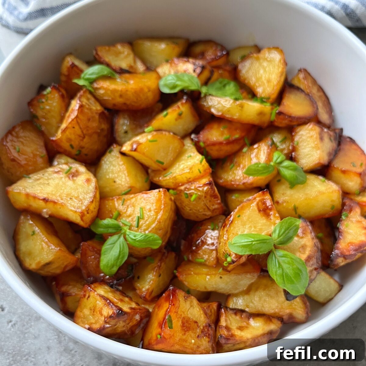 Golden Honey Glazed Potatoes 3 A white bowl filled with roasted potato wedges garnished with fresh green herbs.