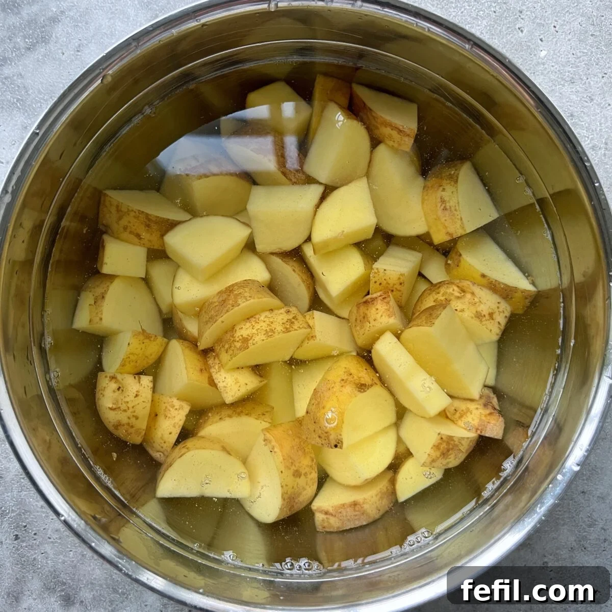 Golden Honey Glazed Potatoes 5 A metal bowl filled with water and chopped potatoes with skins on, soaking in preparation for delicious Honey Roasted Potatoes.