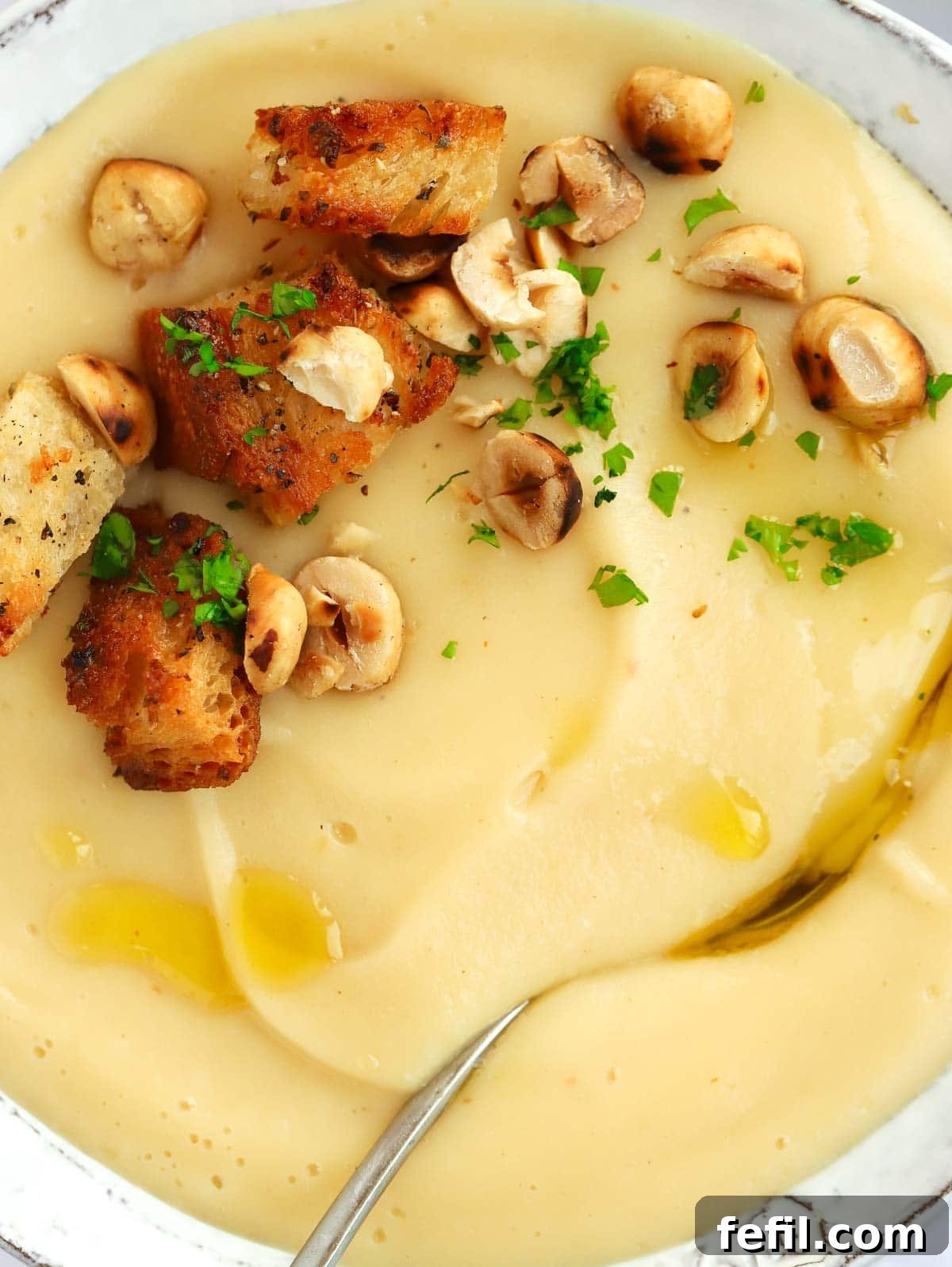 Simple 20 Minute Parsnip Soup 3 A close up of a creamy parsnip soup with croutons and hazelnuts on top, with a spoon ready to serve.
