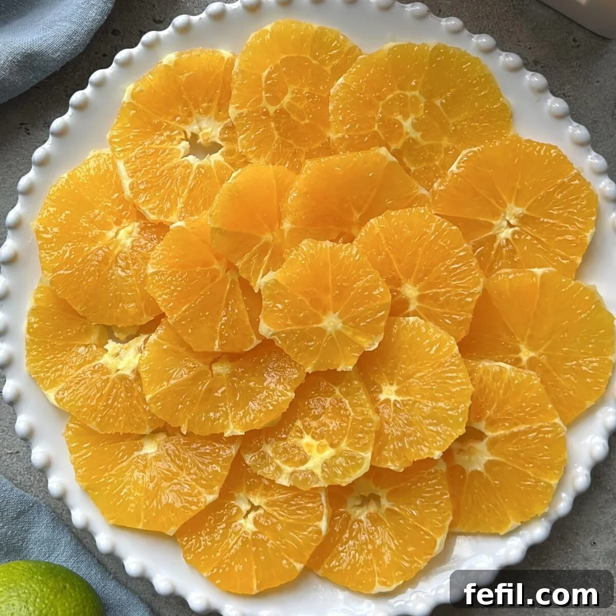 A crisp white plate with a subtle raised beaded edge, meticulously holding neatly arranged, vibrant slices of peeled orange fruit, prepared for a fresh salad.
