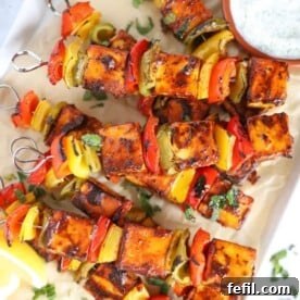 A tray with cooked paneer tikka skewers on and a bowl of raita to the side.