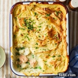 A bird's eye view of a Fish Pie, with a portion missing after being served. Showing the filling of chunky fish, peas and a creamy white sauce.