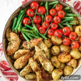 Pesto chicken bake in a dish with green beans, tomatoes and potatoes.