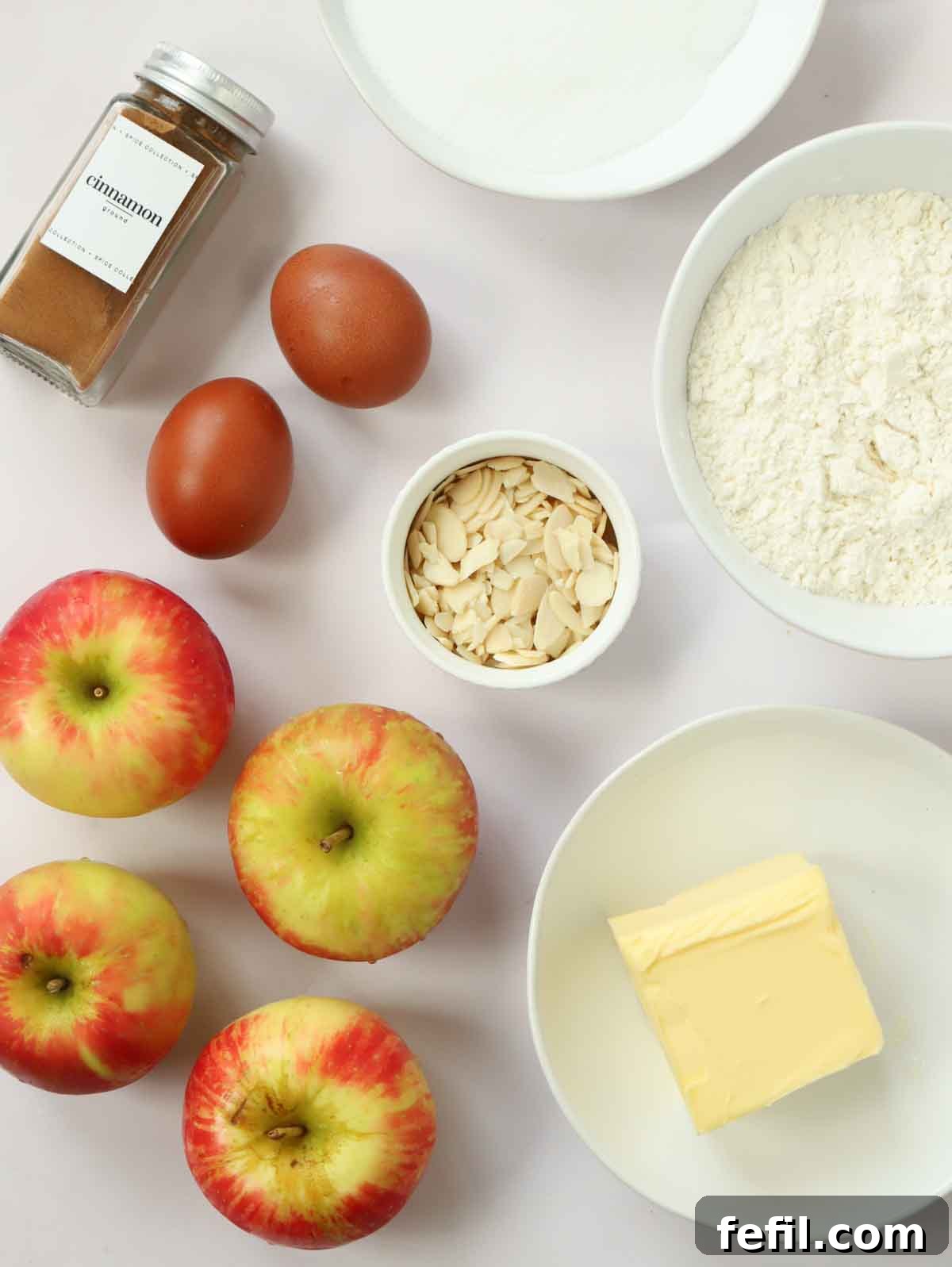 Homestyle Apple Cake 4 All the fresh and pantry ingredients for making a homemade apple cake are neatly arranged on a white kitchen counter.