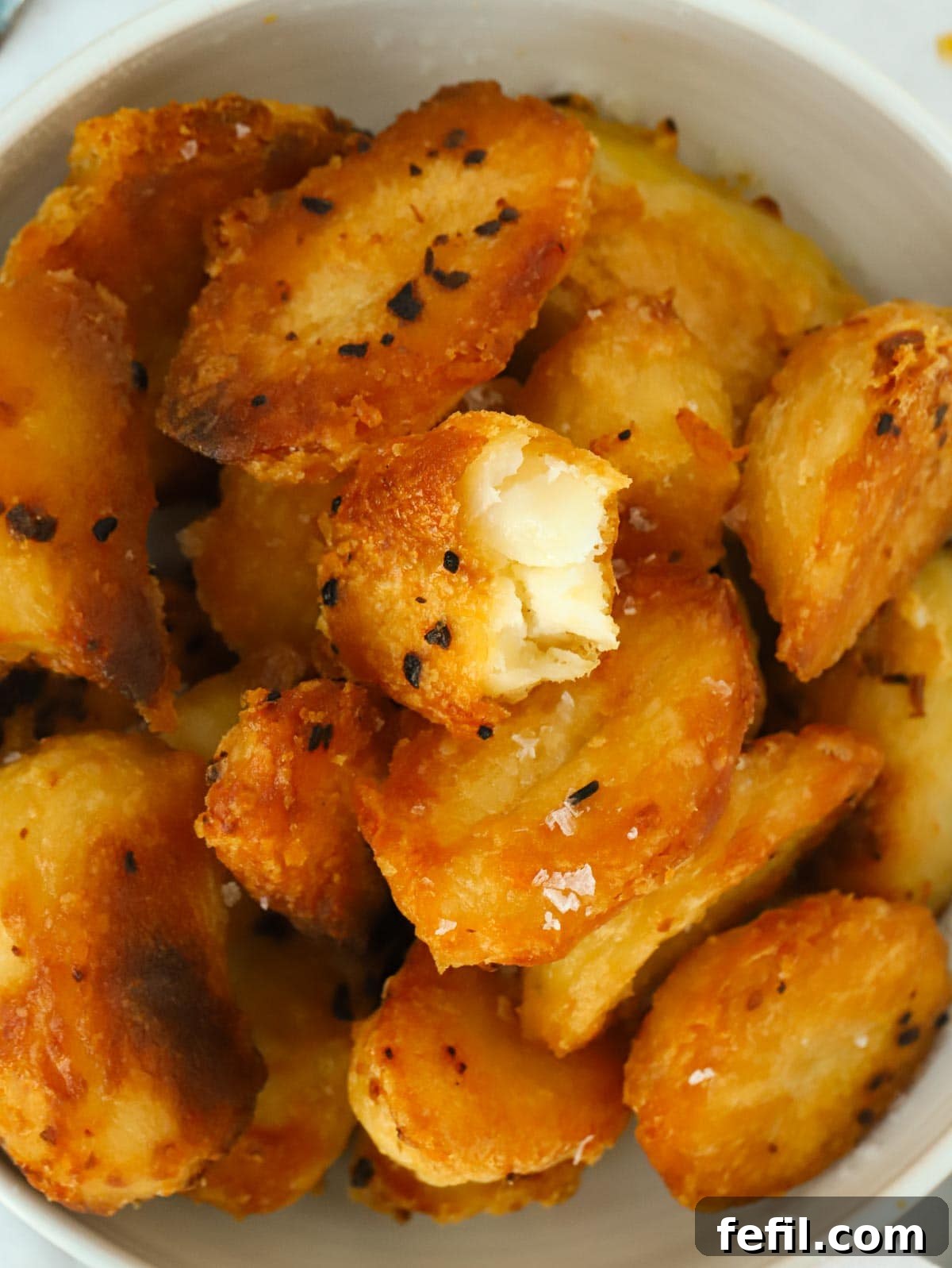 Big close up of a bowl of golden, crispy roast potatoes.