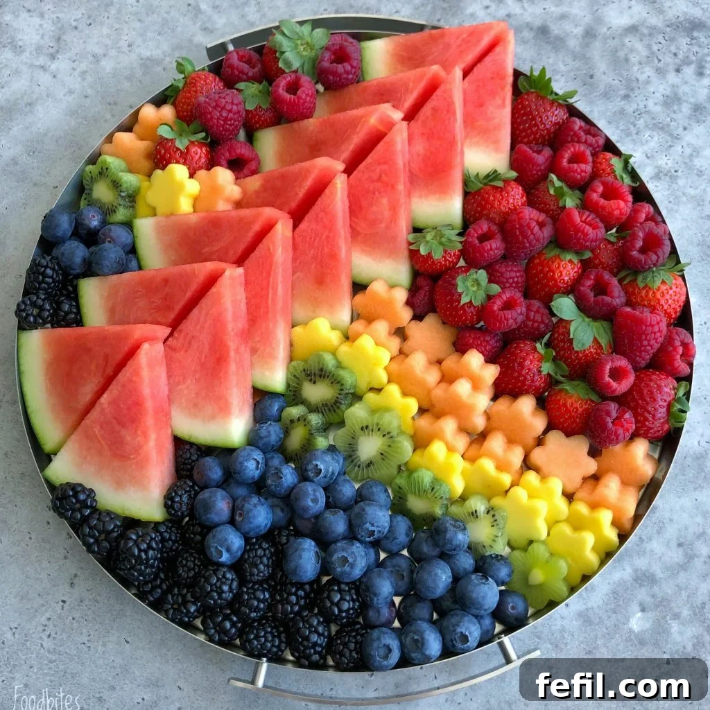 A round platter filled with a vibrant fruit medley—neatly arranged watermelon slices, raspberries, strawberries, blueberries, blackberries, kiwi slices, and flower-shaped pieces of cantaloupe and pineapple.