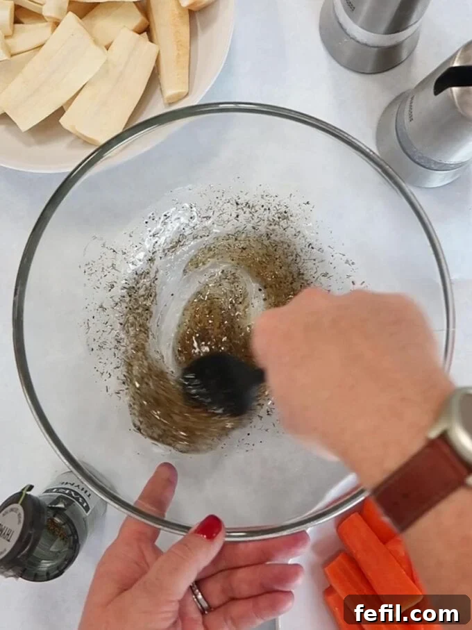 Sweet Honey-Kissed Roasted Roots 5 Step-by-step image showing peeled and chopped carrots and parsnips being tossed in a bowl with oil, honey, and thyme, ensuring an even coating.