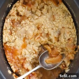 Delicious apple dessert made in a slow cooker, topped with a golden crumble, ready to be served with a spoon.