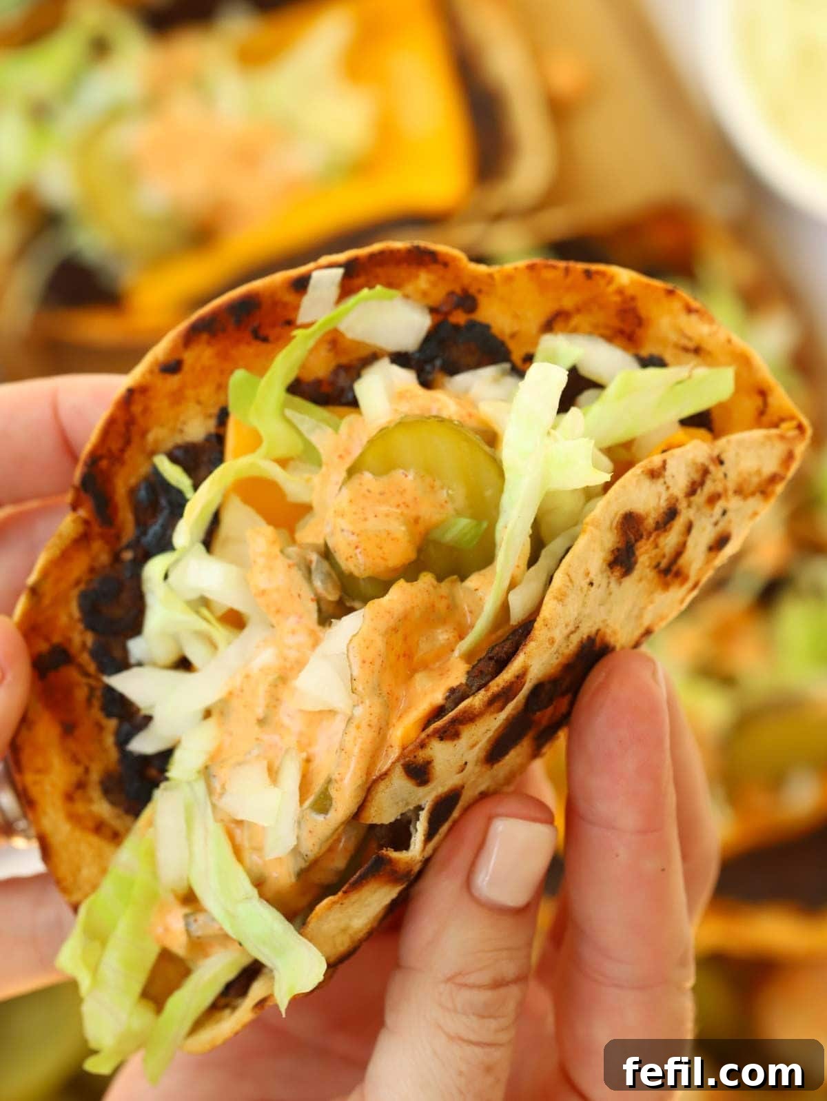 Big Mac Taco Mashup 3 A hand holding a Big Mac Taco, filled with melted cheese, fresh salad, and a generous drizzle of sauce on top.