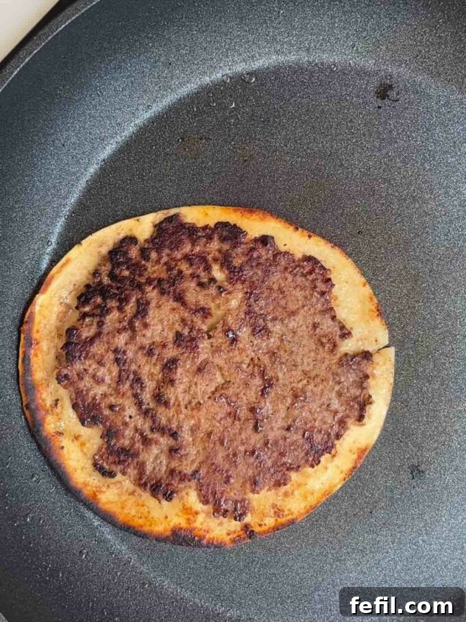 Big Mac Taco Mashup 8 Beef patties on tortilla wraps being fried in a pan, with cheese melting on top, showing the cooking process.