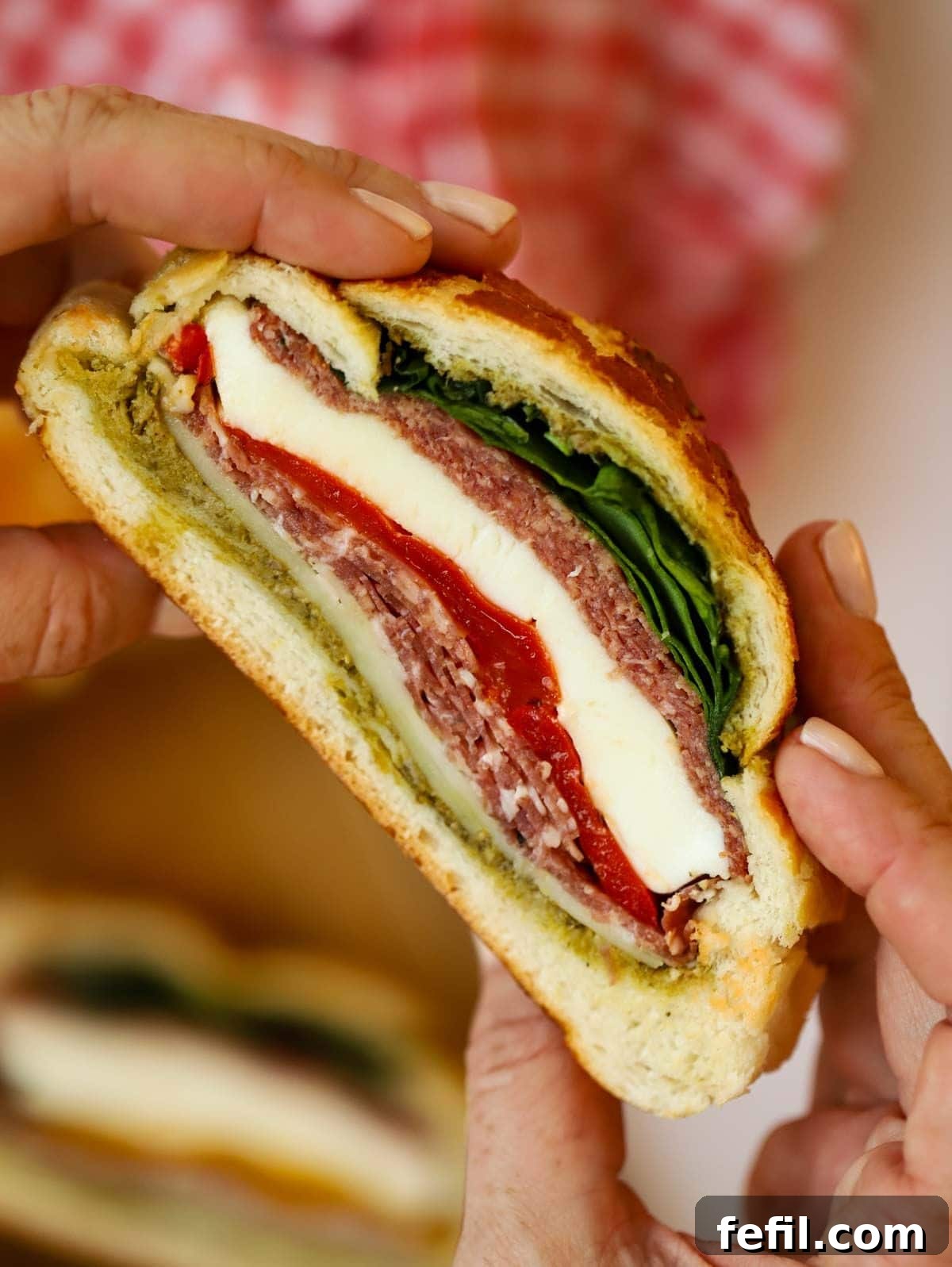 Two hands carefully holding a delicious, fully assembled stuffed Muffaletta picnic loaf, poised for a satisfying bite.