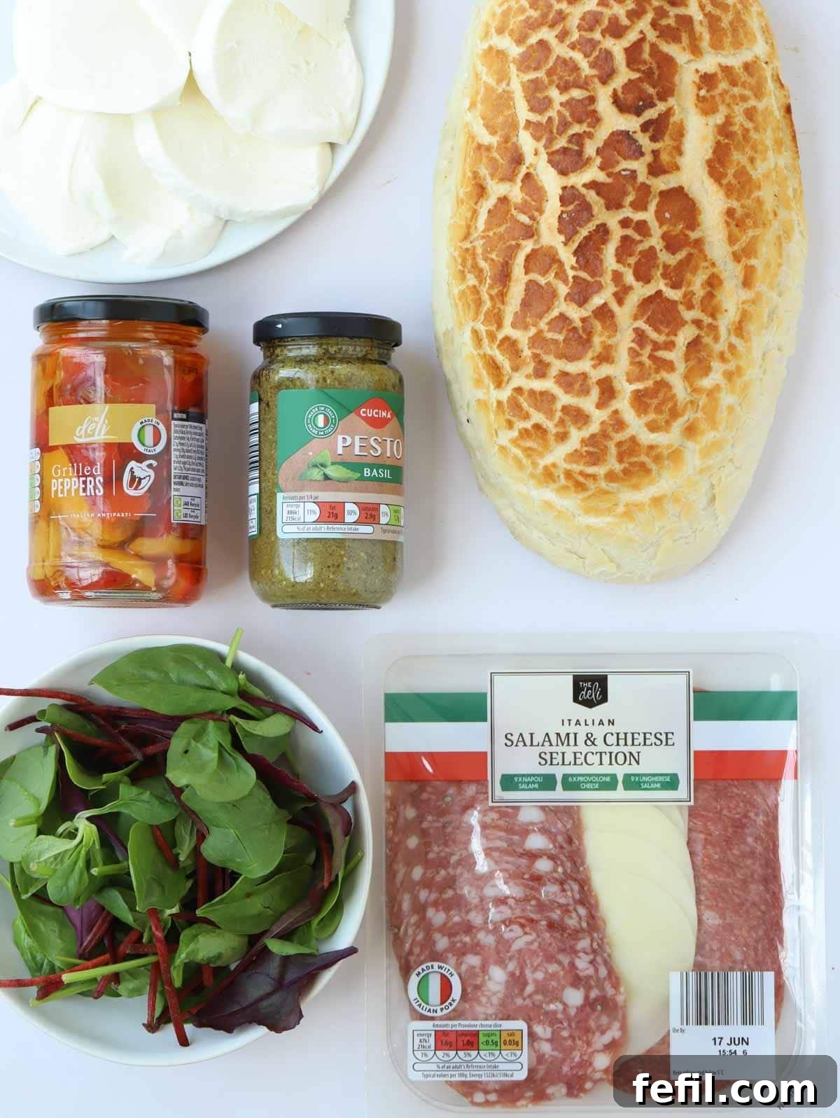 All the fresh and vibrant ingredients for a delicious stuffed picnic loaf, or muffaletta, neatly arranged on a kitchen counter, ready for assembly.