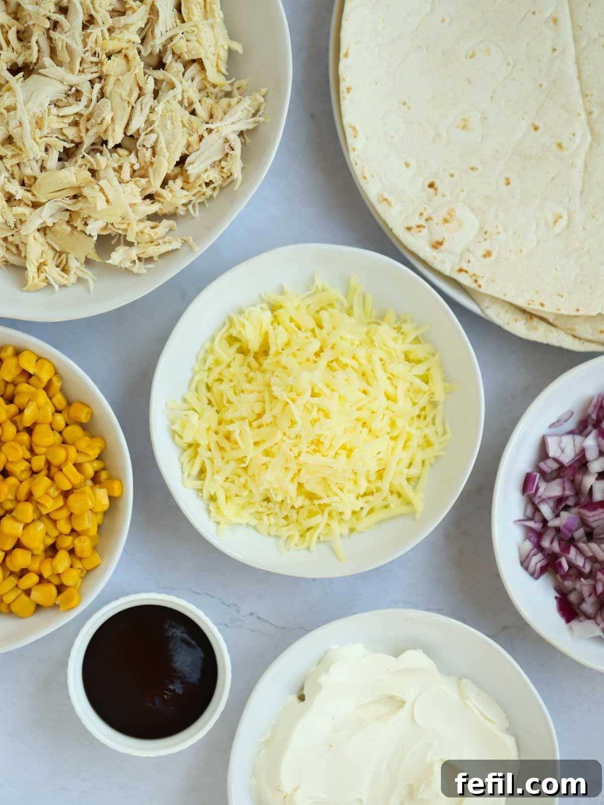 The ingredients for chicken wraps laid out in bowls on a counter top.