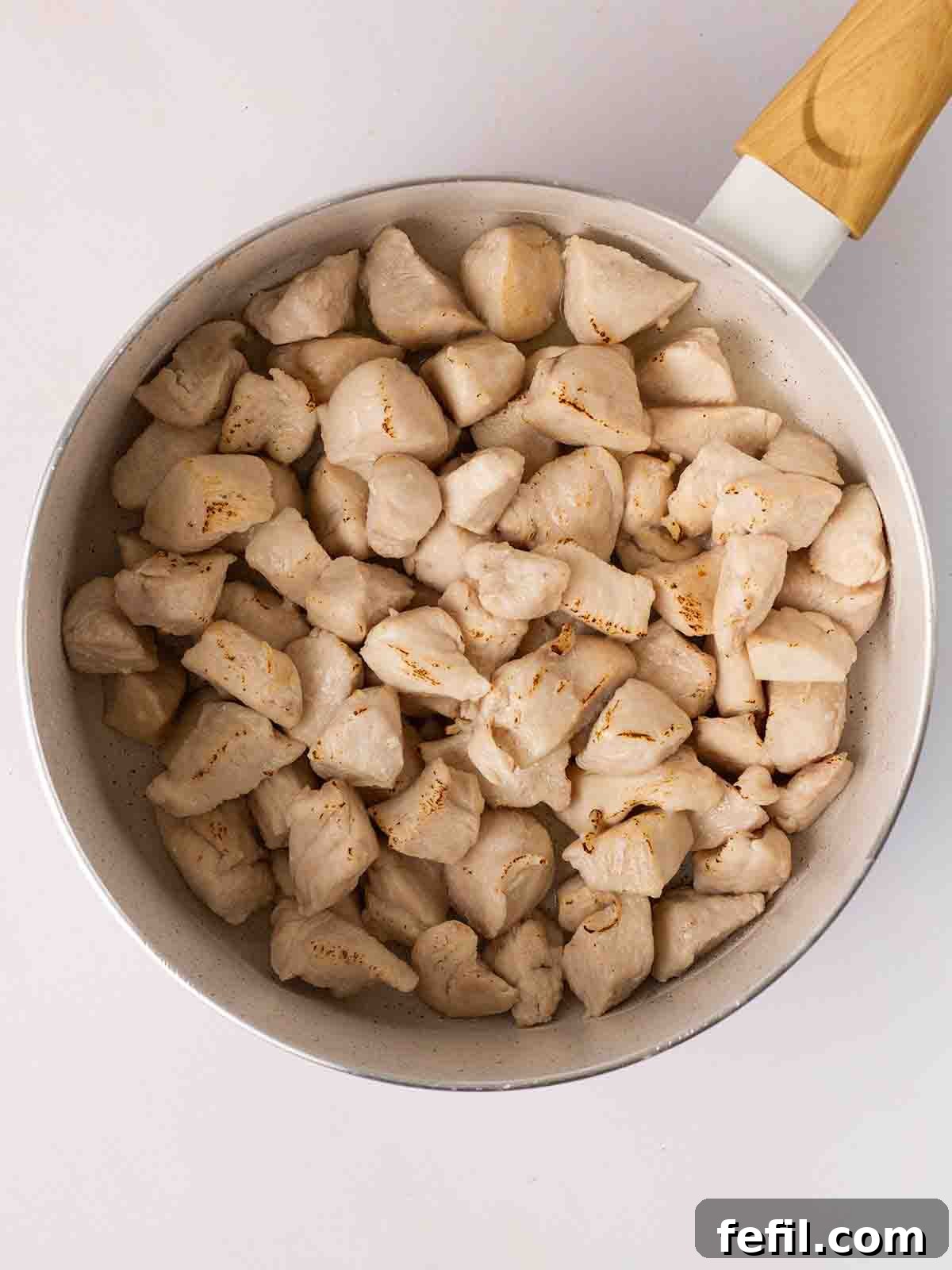 Step 1: Cubed chicken breast pieces frying in a large pan with hot oil, beginning to brown and develop color.
