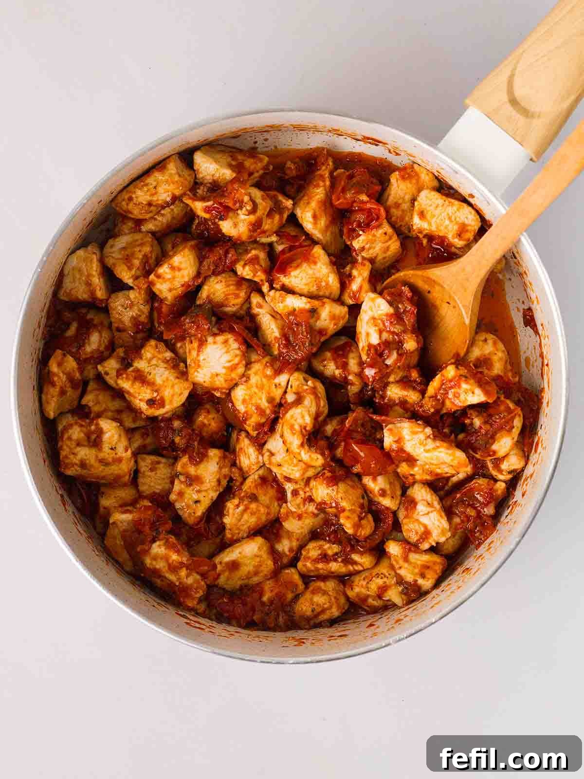 Step 2: Garlic, finely chopped sun-dried tomatoes, oregano, and paprika being sautéed with the browned chicken in the pan, releasing their aromatic flavors.