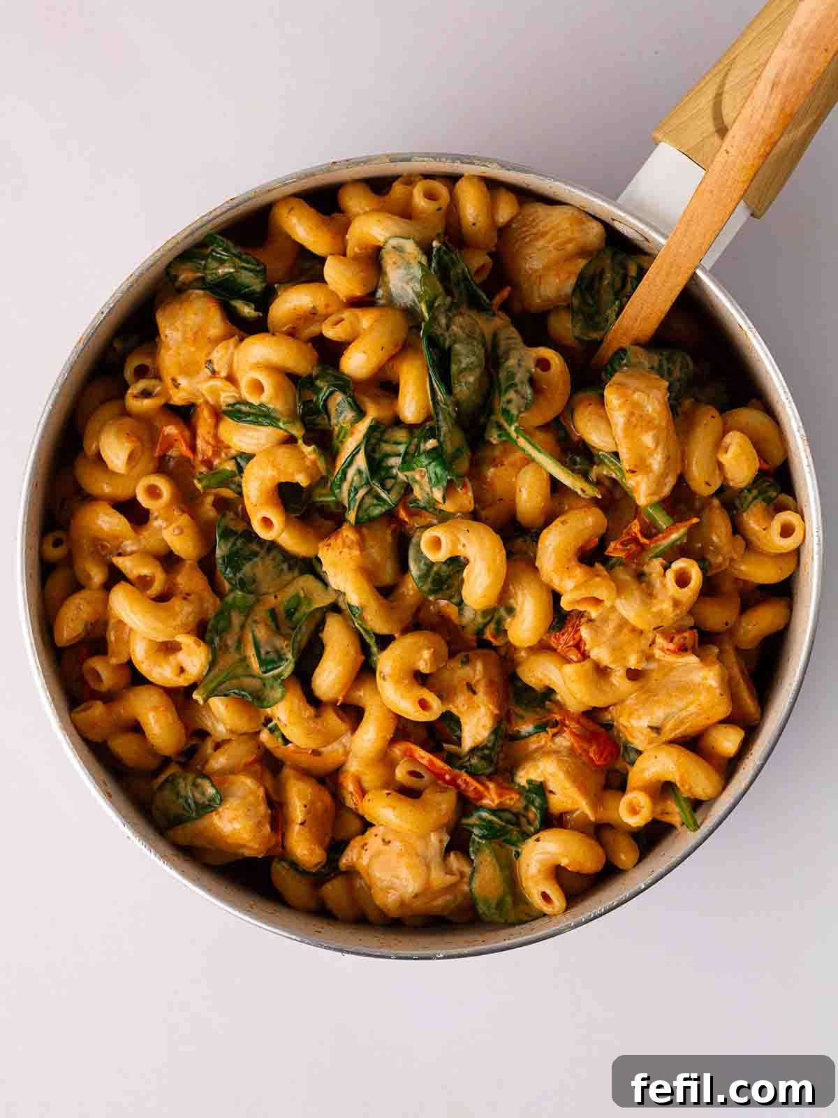 Step 4: Fresh spinach and double cream being stirred into the cooked chicken and pasta in the pan, creating a vibrant, creamy sauce.