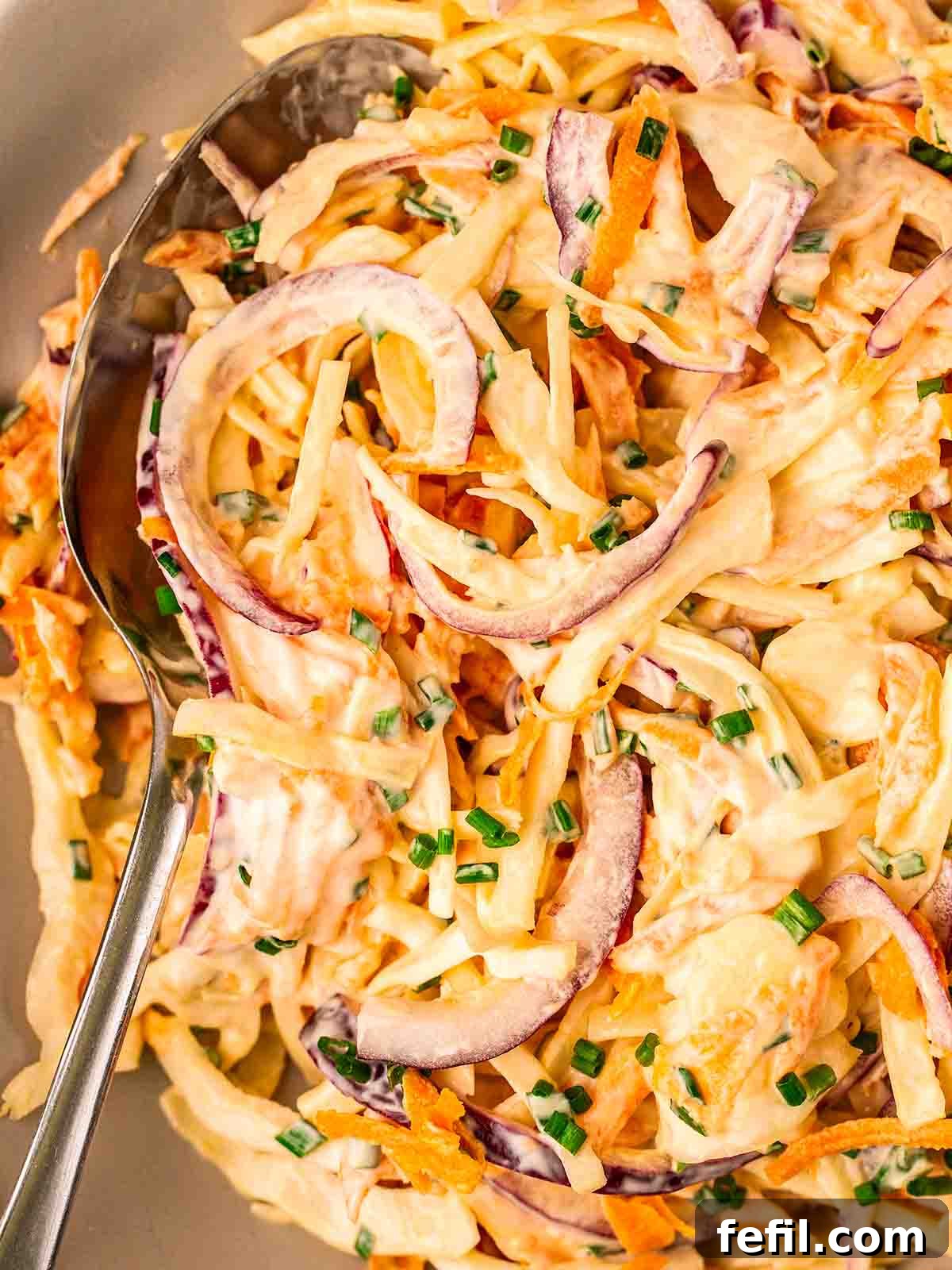 A close-up shot of creamy homemade coleslaw in a bowl with a serving spoon, highlighting its inviting texture.