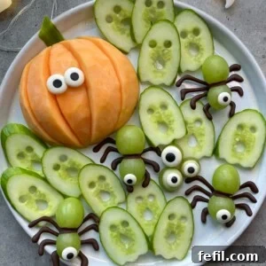 A closer view of the Halloween fruit tray, showcasing intricately carved cucumber ghosts, a charming cantaloupe pumpkin with candy eyes, and playful grape spiders with crunchy pretzel legs, all arranged for festive snacking.