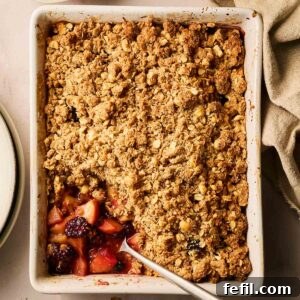 A dish filled with cooked Apple and Blackberry Crumble, with a spoon and a portion missing.