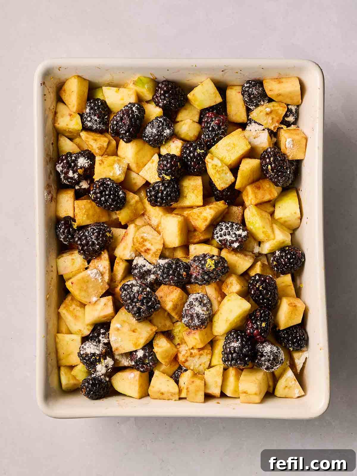 Finely chopped apple pieces and fresh blackberries are mixed in an ovenproof dish, with brown sugar and plain flour sprinkled over the top.