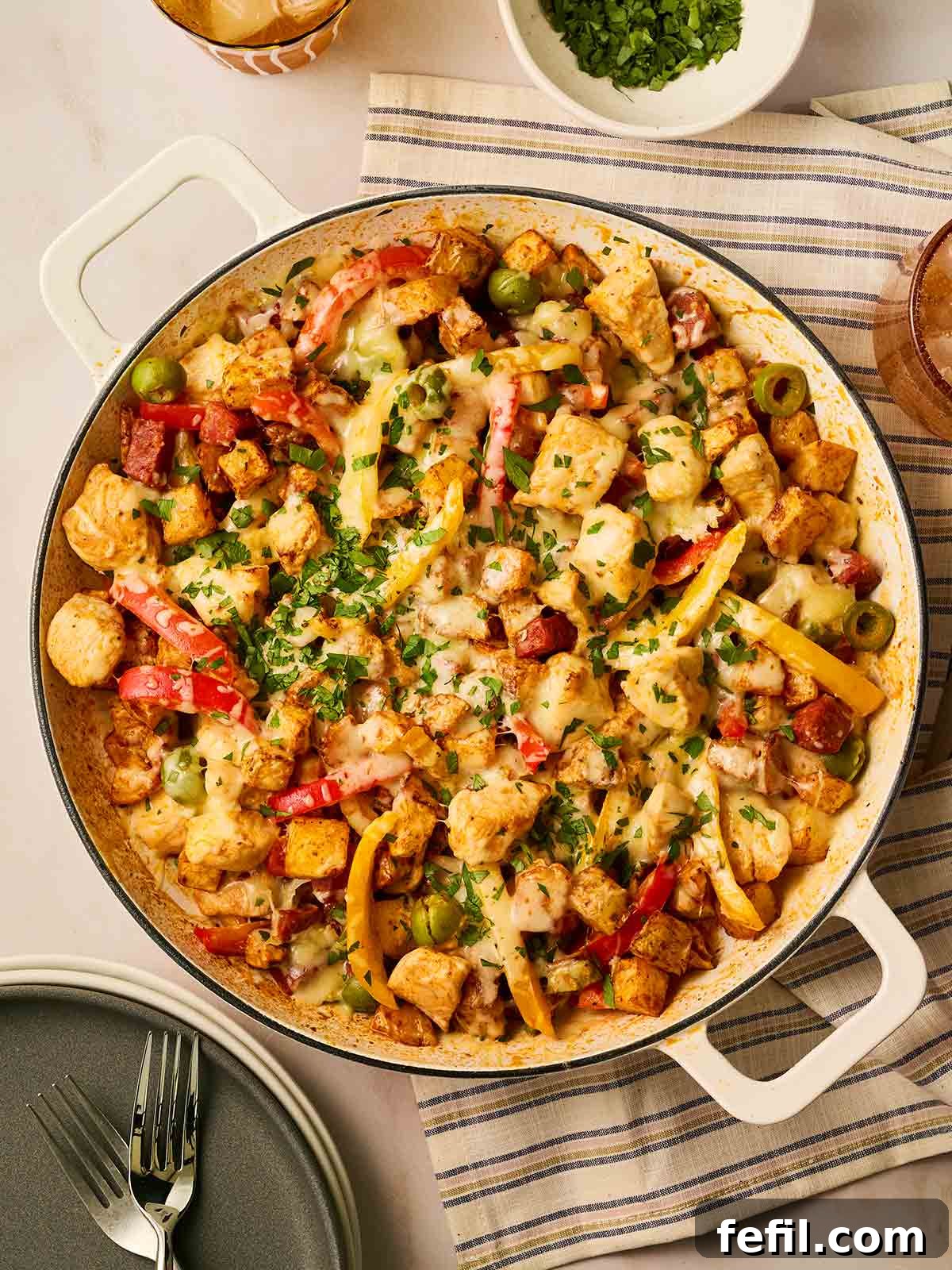 A pan of cooked loaded air fryer potatoes with chicken and chorizo, topped with melted cheese, on a table, ready to serve. The dish is vibrant with red chorizo, golden potatoes, and melted cheese, promising a hearty meal.