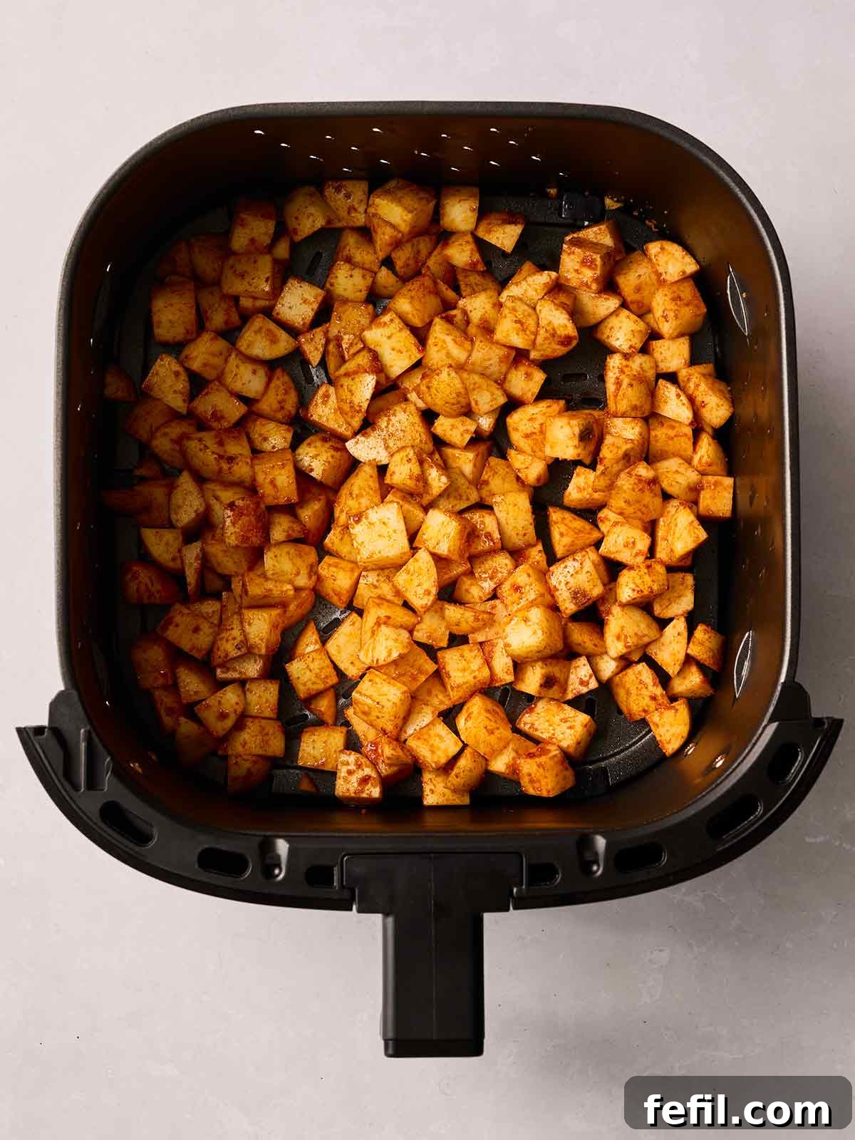 An air fryer basket containing evenly cubed potatoes, thoroughly coated with a blend of sweet smoked paprika and other spices, ready for cooking.