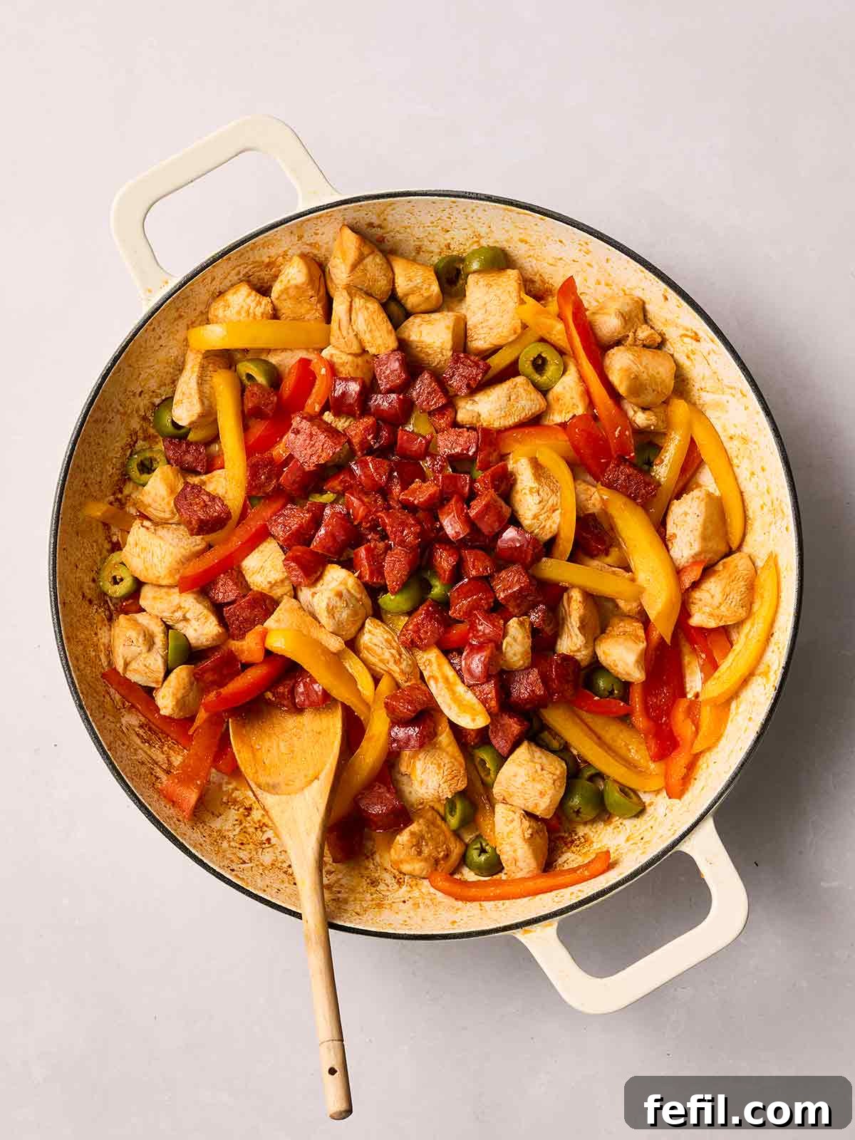 The same pan, now with the cooked chicken, peppers, and olives, having the crispy chorizo reintroduced and stirred in, blending all the savory elements.
