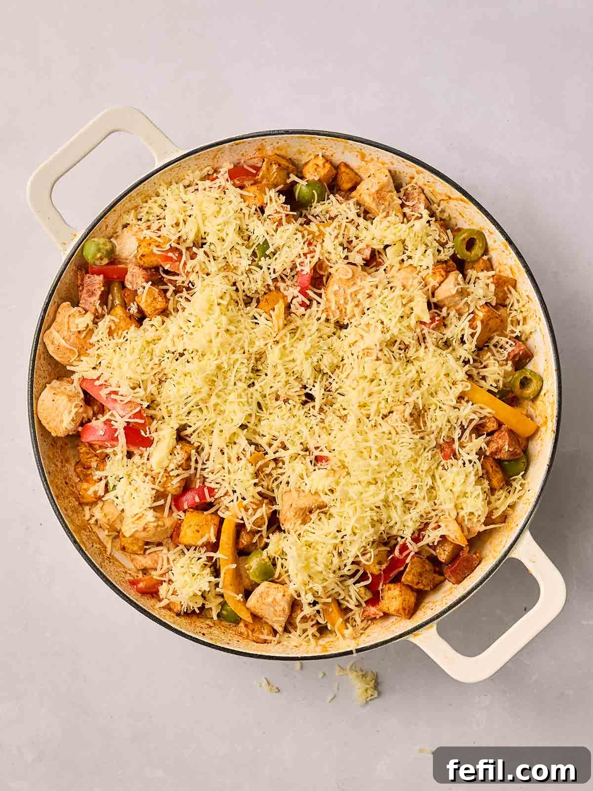 A generous layer of grated cheddar cheese sprinkled over the top of the pan, covering the vibrant mixture of chicken, chorizo, and air-fried potatoes, ready for grilling.
