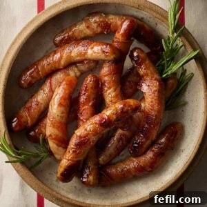 A close up of a dish of Pigs in Blankets decorated with sprigs of rosemary.