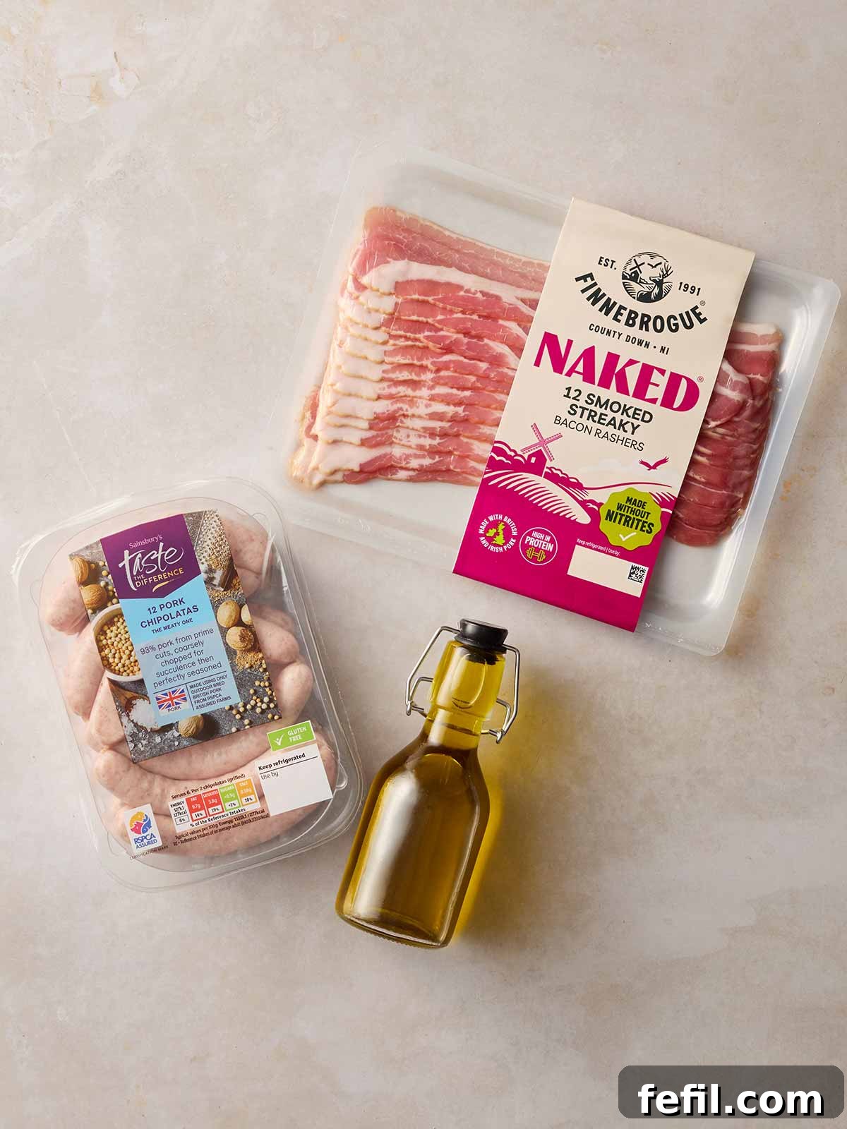 All the necessary ingredients for making homemade Pigs in Blankets, including streaky bacon, chipolata sausages, and a bottle of sunflower oil, neatly arranged on a pristine white surface.