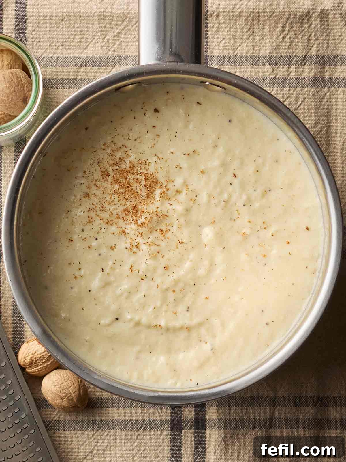 A saucepan filled with the comforting, creamy goodness of homemade Bread Sauce, resting on a table cloth.