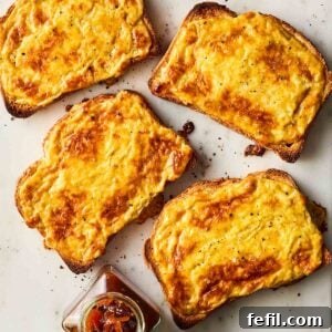 Four slices of Welsh rarebit - cheese on toast with beer - on a white surface, garnished with fresh herbs.