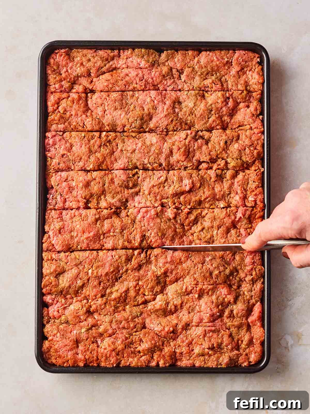 An oven tray with pressed beef mince on and a hand scoring lines into the slab with a knife.
