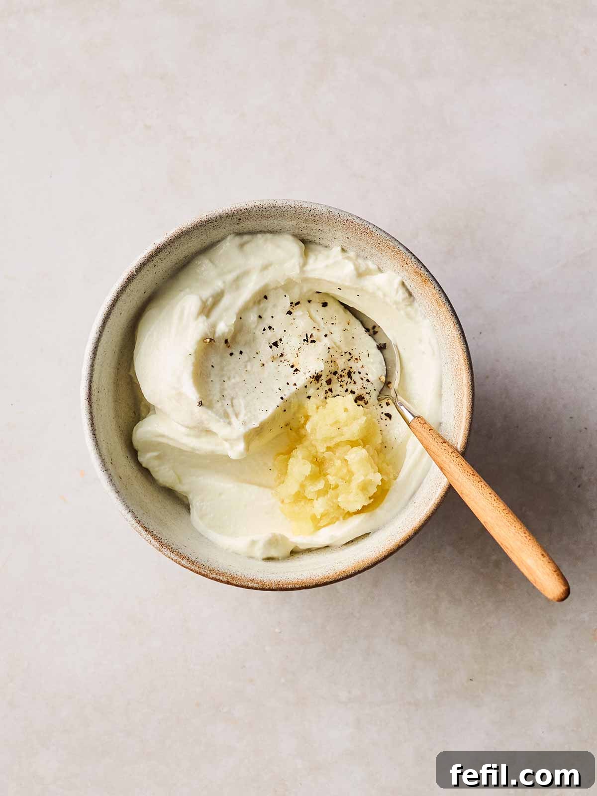 A dish with garlic and Greek yogurt inside, with a spoon to stir.
