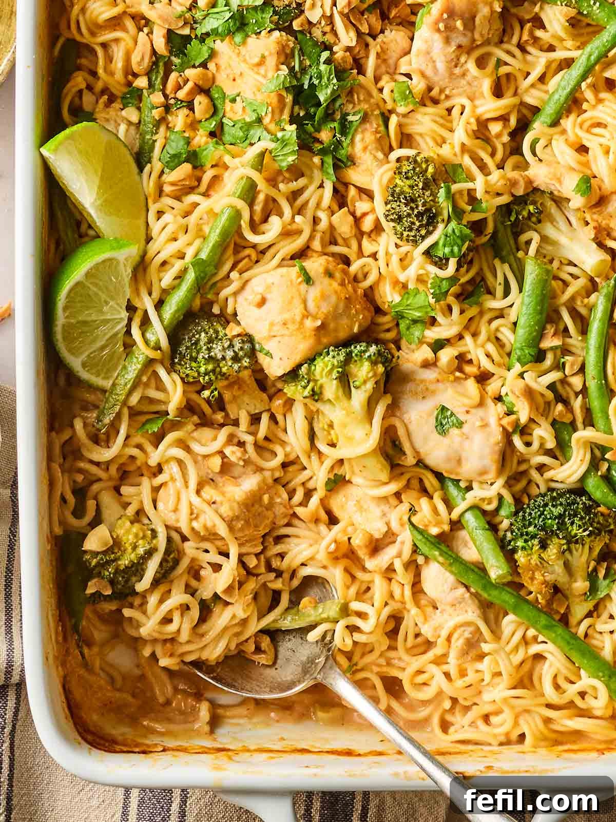 Spicy Peanut Chicken Noodles 3 The edge of an oven dish with spicy peanut butter chicken noodles inside, with a spoon ready to serve.