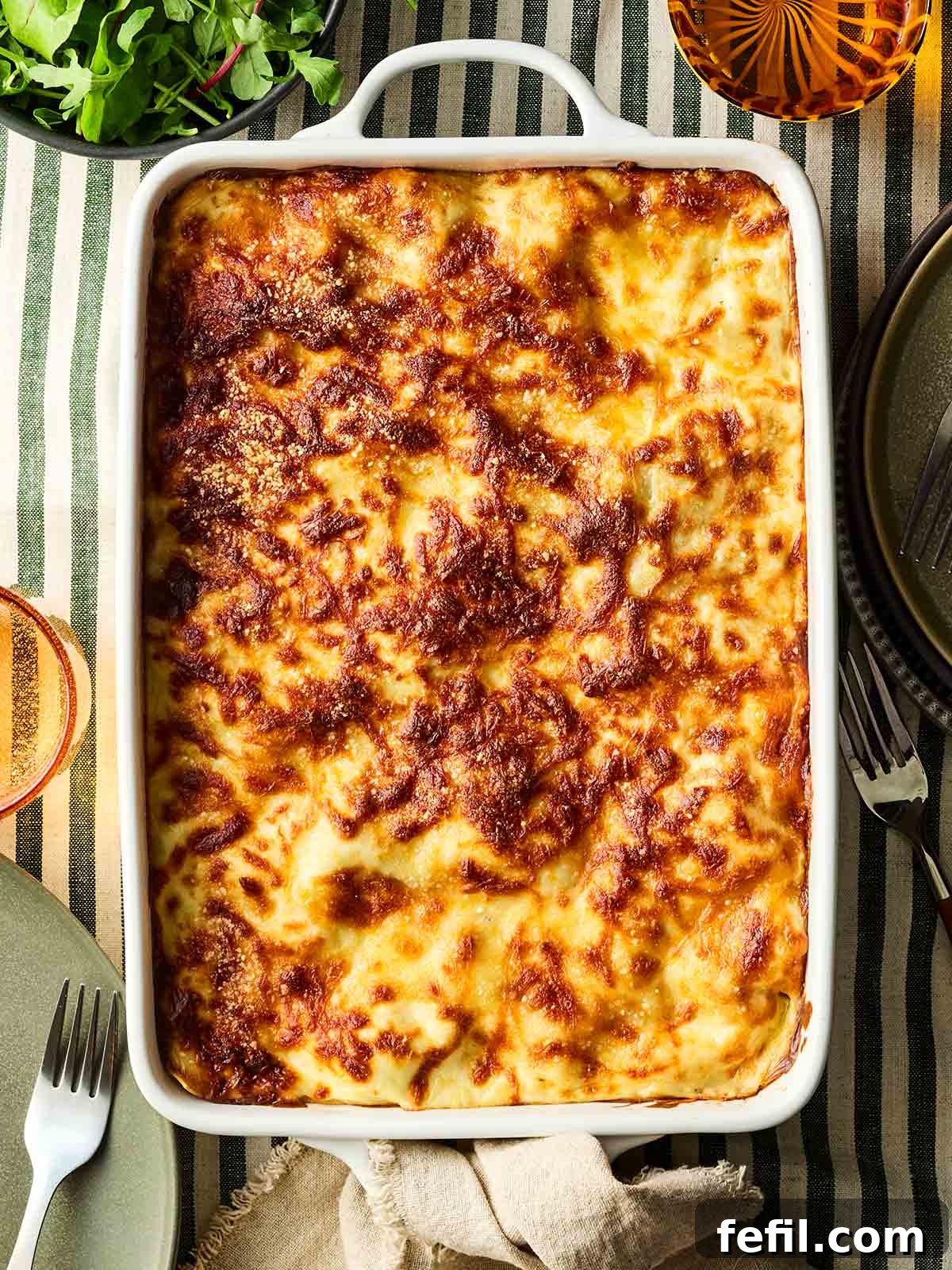The Ultimate Classic Lasagne 3 A bird's eye view of a lasagne in a dish, on a table with stripy green and white tablecloth, ready to serve.